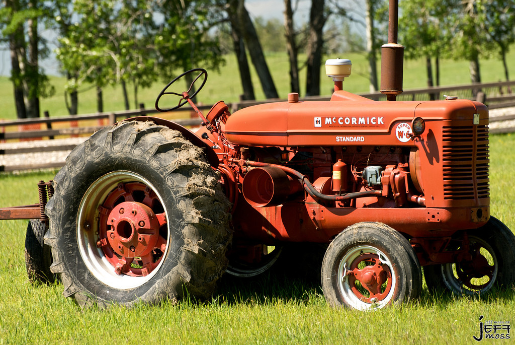 Red McCormick Standard tractor in a grassy field — historic image
