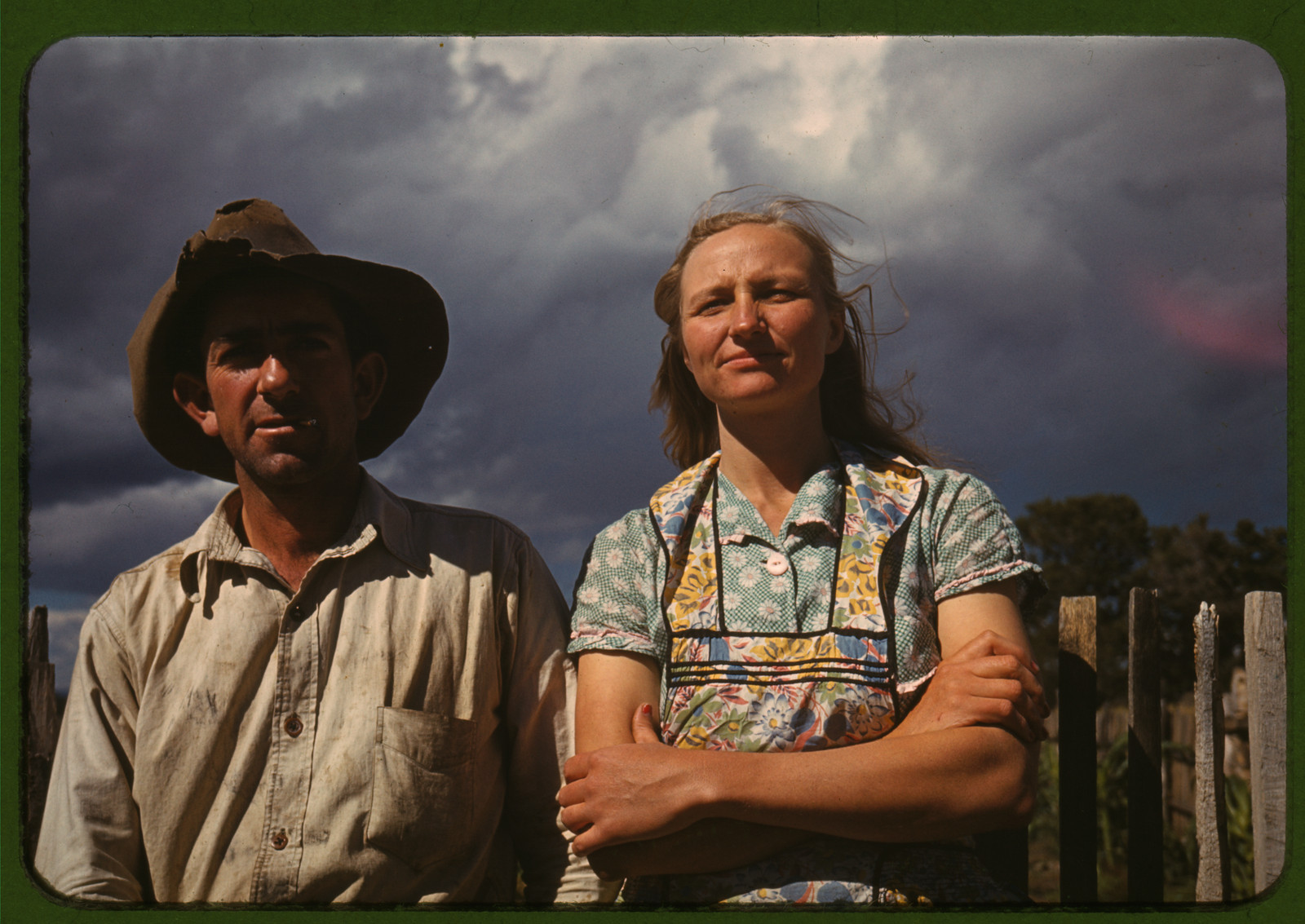 Farm couple standing by a fence under a stormy sky — historic image