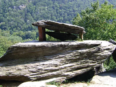 Layered rock outcrop with wooden bench above forested valley