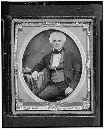 [Alexander Bell, three-quarter length portrait, seated, facing front, with hand on table with tablecloth]
