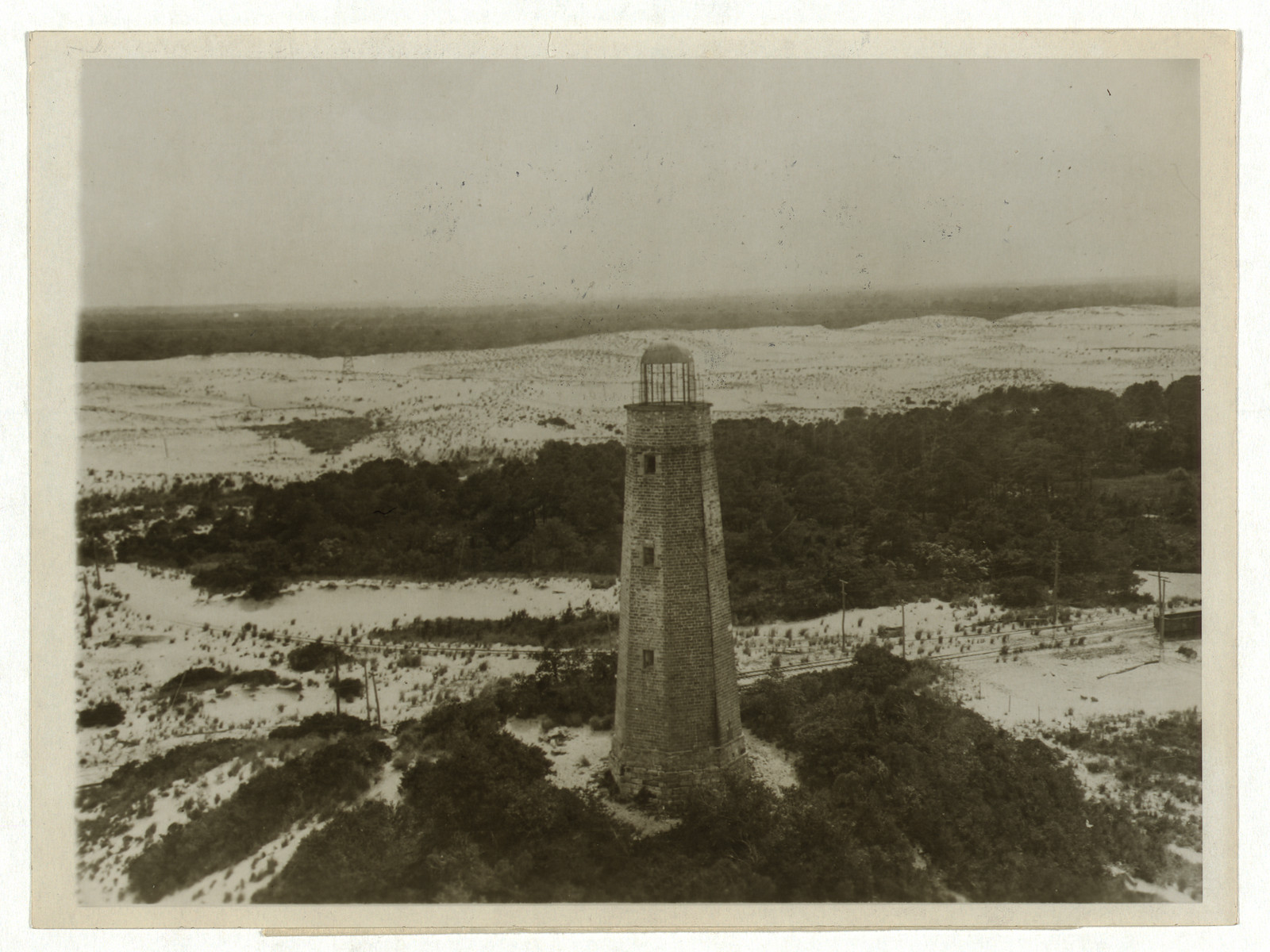 Aerial photograph of a stone lighthouse among dunes and trees — historic photograph