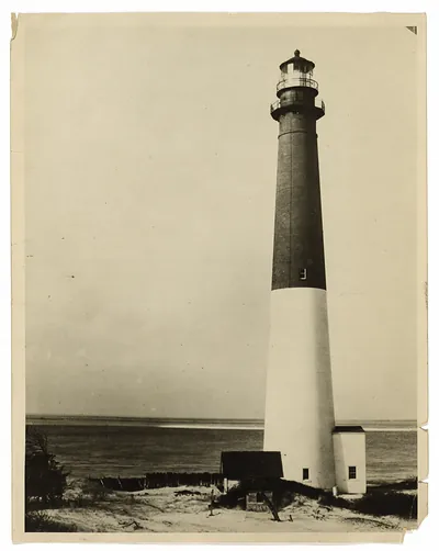Tall lighthouse with dark upper band above sandy shore