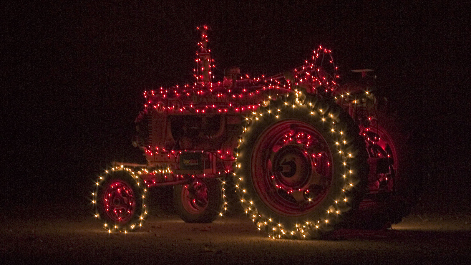 Red tractor decorated with Christmas lights at night — historic image