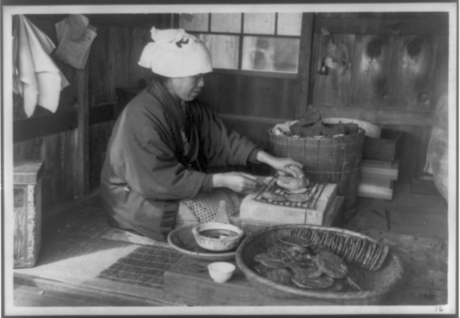 [Japan: woman sitting on floor and baking on grill], [between 1915 and 1925(?)] — historic photograph