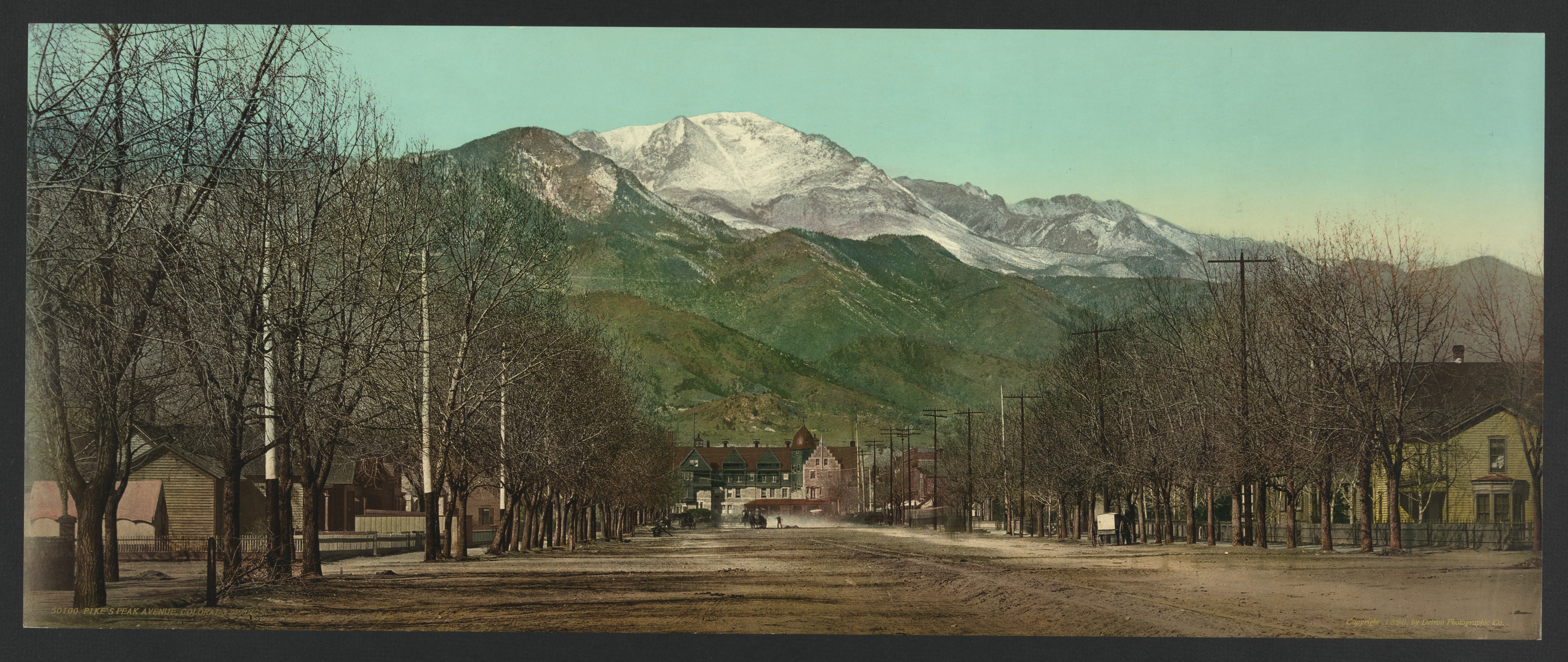 Tree-lined unpaved street with snow-capped Pikes Peak beyond — historic image